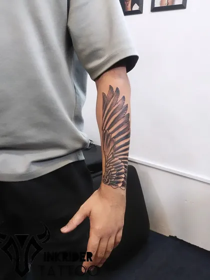 A large, powerful wing tattoo covering the forearm. The detailed shading creates a realistic, three-dimensional effect.