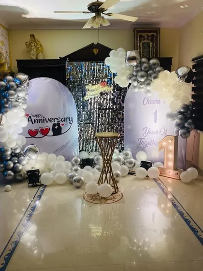 I also create more intimate setups for smaller spaces. This first-anniversary decoration for a living room features custom backdrops, a shimmer wall accent, and coordinated silver and white balloons for a personal celebration.