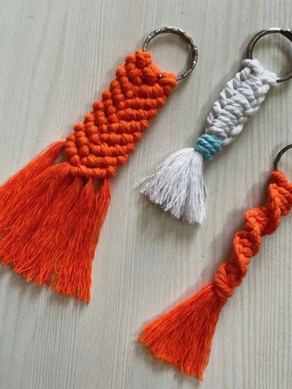 A trio of tassel keychains in a vibrant orange, showing different knotting styles like the spiral and fishtail braid.