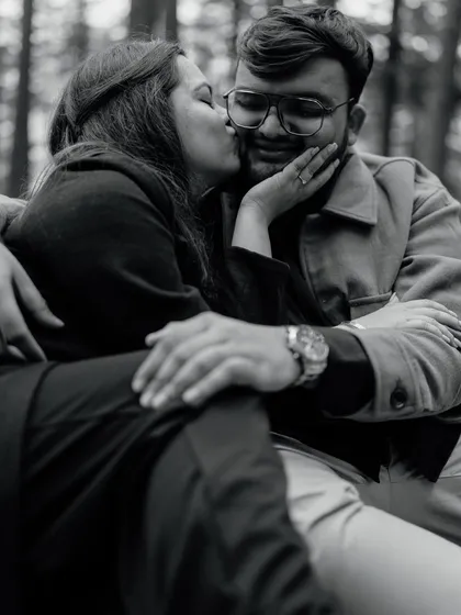 A sweet kiss on the cheek during a Manali forest shoot. This black and white candid shot is full of genuine affection and warmth, a perfect example of capturing real emotions.