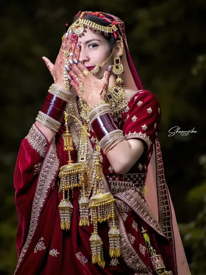 A shy, beautiful pose from the bride. The focus is on her stunning kalire and the intricate details of her wedding attire.