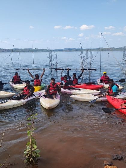 A group of kayakers raises their paddles in celebration after a successful training session at Vani Vilas Sagar.