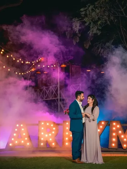A romantic portrait of a couple standing before the 'MARRY ME' sign, enveloped in a cloud of purple smoke. This highlights our expertise in using atmospheric effects for night photography.