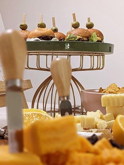 A close-up view of a cheese board, showcasing a variety of textures from creamy to crumbly, paired with mini burgers in the background. It's all about offering delightful contrasts.
