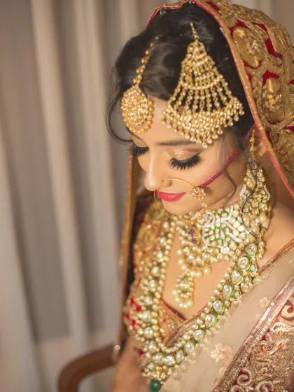 A detailed portrait of a bride in her magnificent red and gold lehenga. The close-up on her jewelry and makeup highlights the exquisite details of her bridal look.