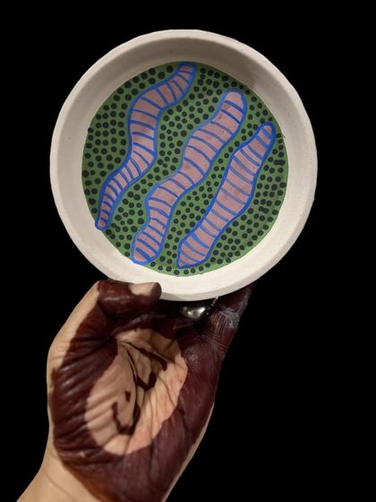 A hand-painted plate with a playful pattern of green dots and pink-and-blue worms. I don't take my patterns too seriously; the goal is to create something that makes you smile.