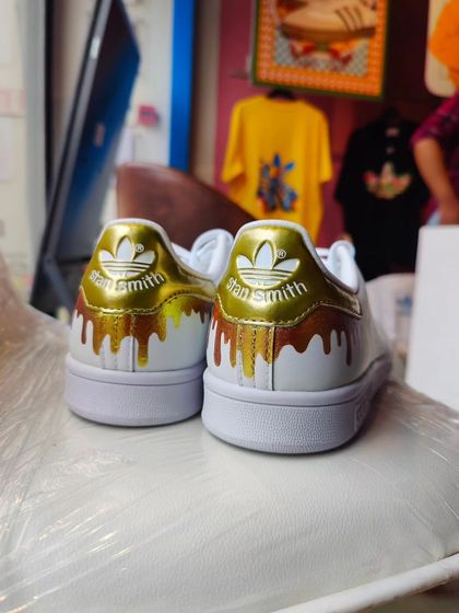 A pair of classic Stan Smiths with a custom gold drip effect on the heel, painted live at the Adidas store.