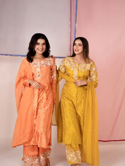 A cheerful, bright shot for an e-commerce catalog, featuring two models in colorful ethnic suits. The image is clean, well-lit, and focuses on the garments.