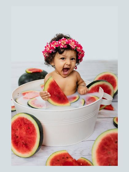 A baby girl laughs with delight while holding a slice of watermelon in her milk bath. Her joyful expression is the highlight of this fun and fruity photoshoot.