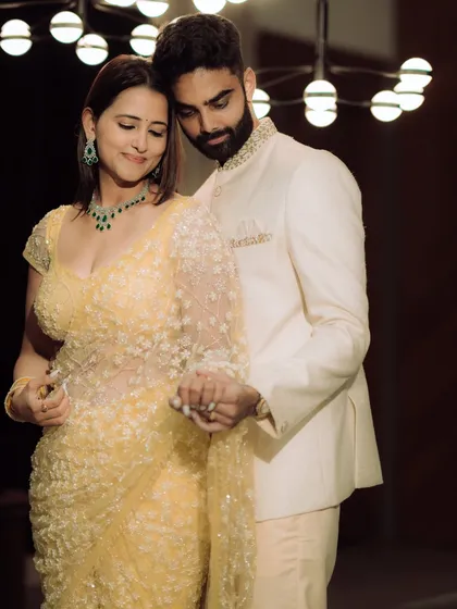 A classic, elegant portrait from an indoor engagement shoot. The couple holds hands, their pose exuding confidence and grace under the soft glow of a contemporary light fixture.