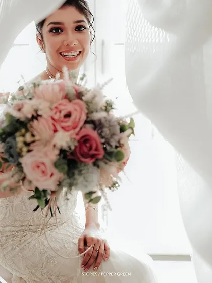 A lovely portrait of the bride peeking through curtains, her bouquet adding a splash of color to the dreamy scene.