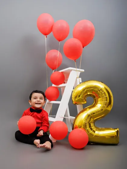 A happy two-year-old plays with red balloons next to a giant number "2" foil balloon.