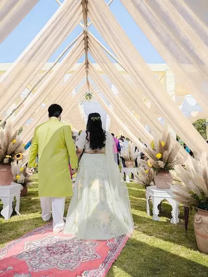 The couple's entrance at their bohemian-themed Mehendi, walking down a carpeted aisle through a tunnel of soft drapes and pampas grass.