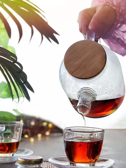 An action shot of tea being poured from a modern glass teapot into a cup, creating a sense of warmth and hospitality.