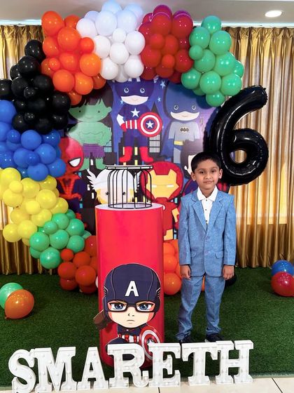 A full Avengers-themed birthday setup for a 6th birthday. The backdrop features multiple superheroes, surrounded by a colorful balloon arrangement and a large number '6' balloon.