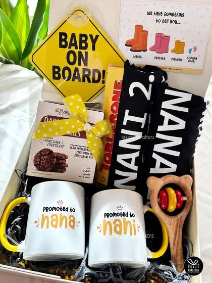 This pregnancy announcement hamper was designed for the 'Nana & Nani'. It features personalized mugs, a 'Baby on Board' sign, and a custom onesie, all packed with love.