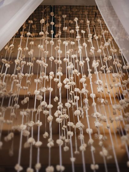A curtain of delicate, handcrafted white flowers (moti) hanging within the Varmaala mandap. This intricate detail adds texture and a sense of ethereal beauty to the backdrop.