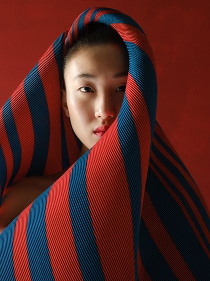 A close-up portrait where the model is enveloped by the striped pleated fabric. This shot focuses on the texture and color of the textile as a primary design element.