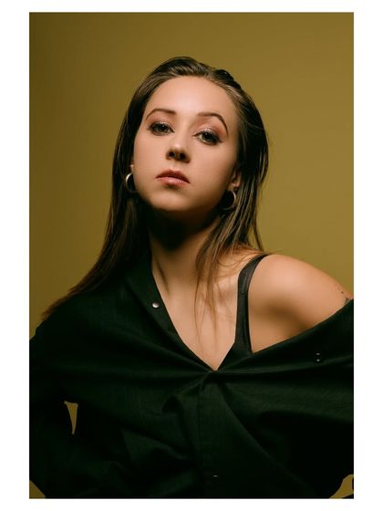 A moody and intense portrait with a dark, olive-green background. The lighting is focused on the model's face, creating a dramatic and captivating image.