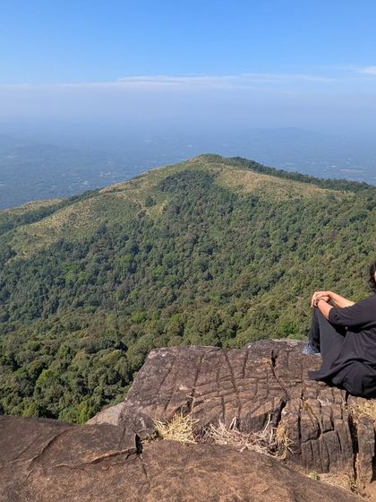 A trekker sitting on a rock and enjoying the panoramic view from the Kurinjal trail.