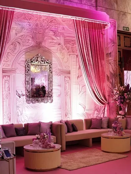 A luxurious lounge area bathed in pink light, with a beautifully detailed backdrop, plush sofas, and elegant floral arrangements on the center tables.