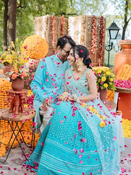 A romantic portrait of the couple seated amidst their Haldi decor, showered in delicate pink petals.