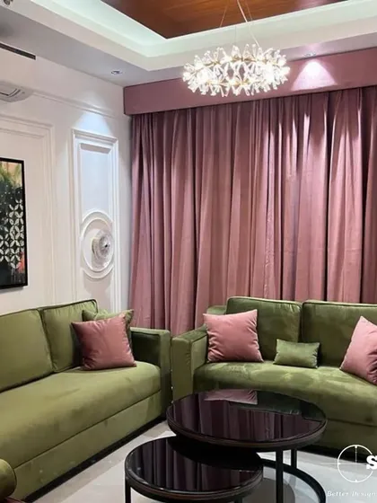 Another angle of the colorful living room, showing the interplay between the olive sofas and the long, flowing pink curtains. The crystal chandelier adds a touch of glamour to the eclectic space.