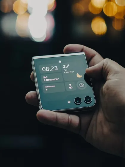A lifestyle product shot of the Samsung Galaxy Z Flip 5. I focus on capturing the device in real-world scenarios, highlighting its design and user interface against an atmospheric, out-of-focus city background.