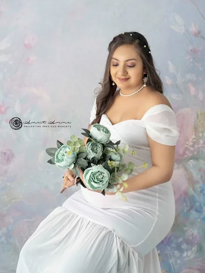 A serene seated portrait. Holding a bouquet of flowers, the mother to be looks peaceful and radiant against the soft, artistic backdrop.