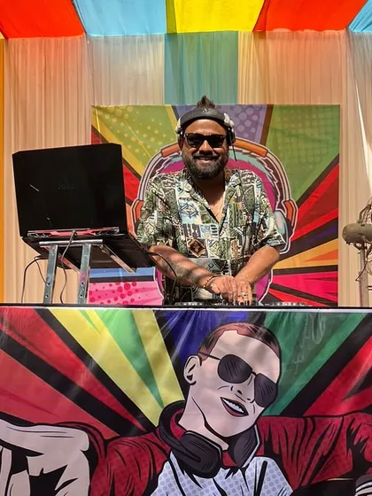 A cool, pop-art style photo from a daytime event. The colorful backdrop and custom DJ booth art show the fun, vibrant atmosphere of the party.