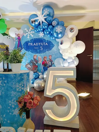 A close-up of the Frozen side of the party, with a blue and silver balloon arch, snowflake details, and a large light-up number '5'.