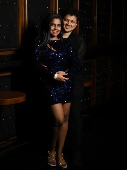 A full-length portrait of the couple at their cocktail party. The dramatic lighting highlights them against the dark, stylish venue.