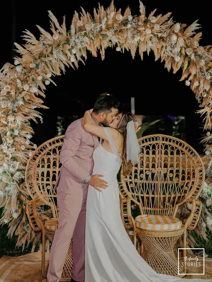 A passionate kiss seals the promise under a beautiful bohemian pampas grass arch at a Goa beach wedding. This frame captures the peak emotion and stunning decor of a modern coastal ceremony.