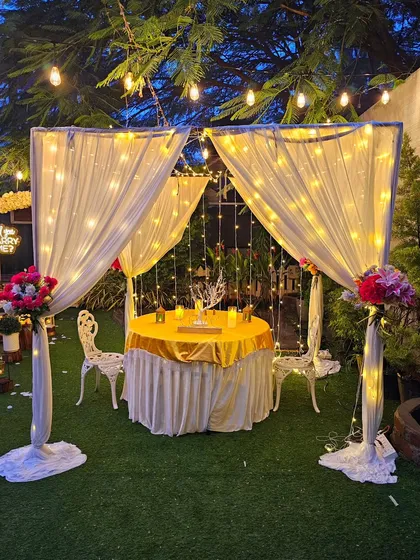 I can create an intimate and elegant dinner for two with this beautiful cabana setup. Draped in white fabric and wrapped in warm fairy lights, it provides a private, romantic space in your own backyard, complete with a beautifully set table and floral accents.