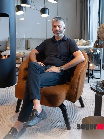 A portrait of me, Ar. Sumit Dhawan, in a well-appointed interior. The space features a modern freestanding fireplace and a sculpture of Atlas, reflecting a design philosophy that balances artistic expression with functional comfort.