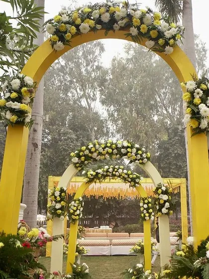 The yellow floral arches create a beautiful, layered entrance, inviting guests into the garden where the Haldi ceremony will take place.