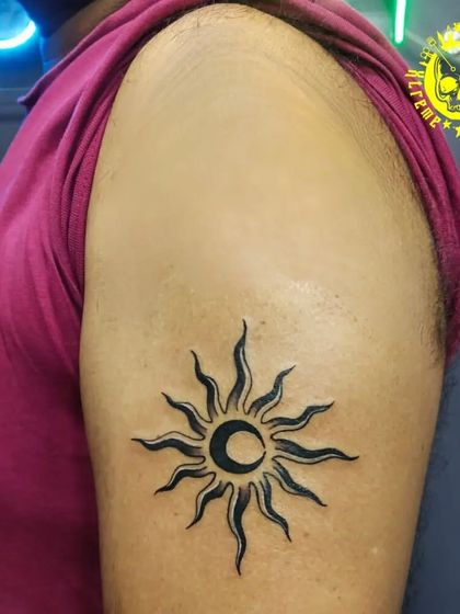 A tribal-style sun and moon tattoo on the upper arm. This design represents the union of opposites, like light and dark, in a bold, graphic style.