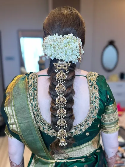 A detailed view of a traditional South Indian bridal braid, showcasing the beautiful contrast between fresh jasmine flowers and intricate gold temple jewelry hair accessories (Jadanagam). This style is a testament to timeless bridal beauty.