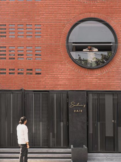A closer look at the brick facade and circular window of our Dwarka residence. This shot captures the texture of the terracotta bricks and the way the window frames a view from within, blending modern design with traditional materials.