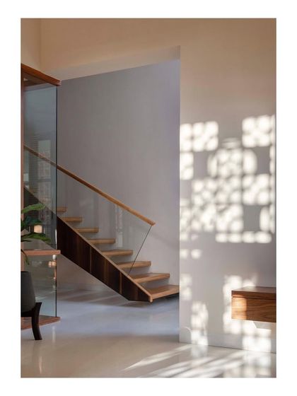 Light filtering through a perforated screen casts intricate shadow patterns on the wall next to the staircase. This detail illustrates our approach to using architectural elements to create dynamic, ever-changing light conditions within a home.