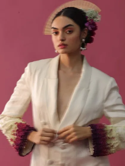 This close-up on a double-breasted blazer highlights the custom, textured sleeve details. The styling, complete with a floral and fan headpiece, embodies a fusion of traditional artistry and modern, avant-garde fashion.