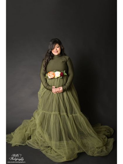 A full-length view of the olive green gown with a tulle overlay. This classic studio pose beautifully showcases the dress and the baby bump.