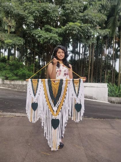 Holding our green, mustard, and white macrame wall hanging. This piece is a perfect example of how we blend colors to create a bohemian and artistic vibe.