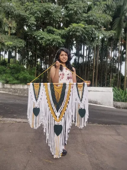 Holding our green, mustard, and white macrame wall hanging. This piece is a perfect example of how we blend colors to create a bohemian and artistic vibe.