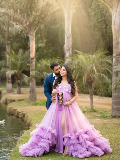 A beautiful outdoor family moment. This couple shares a sweet moment by the water, holding up their ultrasound photo. The vibrant purple gown looks stunning against the lush green park setting.