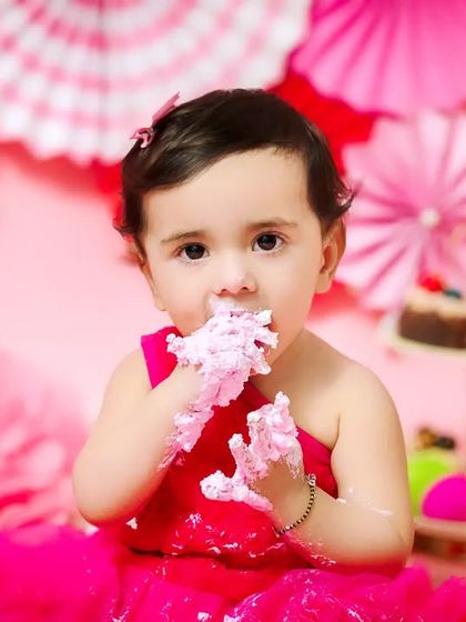 A close-up of a baby girl enjoying her cake smash, with pink frosting all over her hands and face. These messy moments are the most fun to capture.