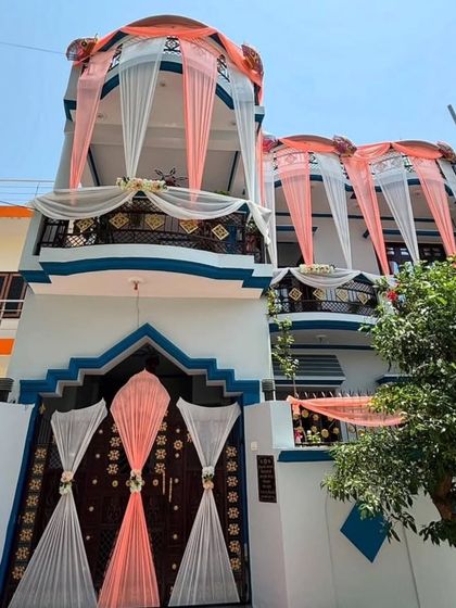 A simple and elegant exterior decoration for a home wedding. The peach and white drapes on the balconies and gate create a clean and festive look.