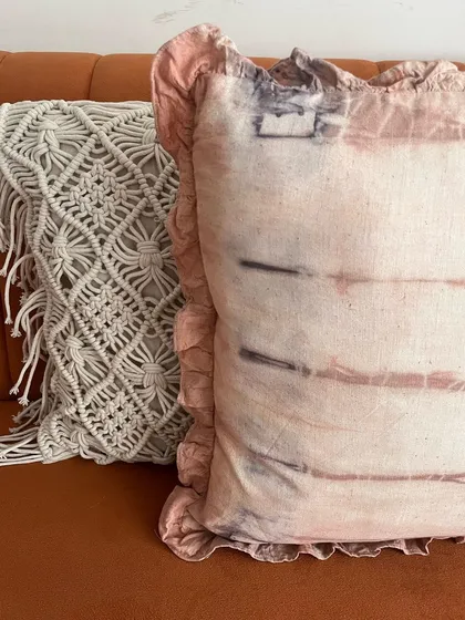 This ruffled pillow cover brings a soft, natural touch to your home. It was dyed using plant-based pigments, giving it a unique, earthy pattern. It sits here next to a macrame cushion, showing how handmade textures can create a warm and inviting space.