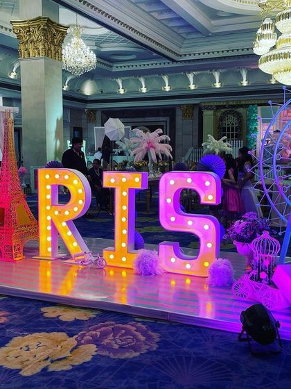 Large, illuminated marquee letters spelling 'PARIS', with a model of the Eiffel Tower and a Ferris wheel, creating a spectacular stage and photo backdrop.