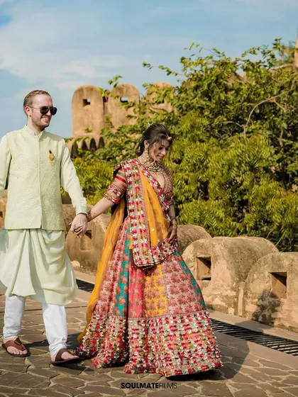 A couple walks hand-in-hand at a historic fort, the bride in her vibrant Mehendi outfit. This shot beautifully combines a destination's grandeur with the colors of a wedding ritual.